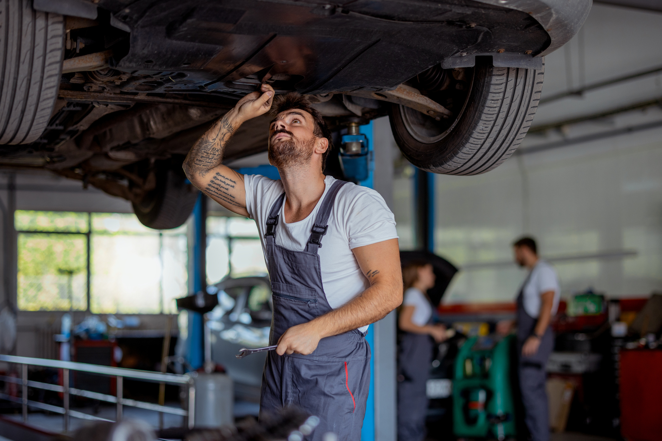 A focused automotive technician works under a lifted car in a clean and organized repair shop, demonstrating his commitment to quality service.
